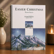 Music book titled 'Easier Christmas Piano Solos' by Jason Tonolioli on a wooden surface with decorative elements.