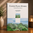 Music book titled 'Easier Piano Hymns' by Jason Tonioli on a wooden surface with a scenic cover